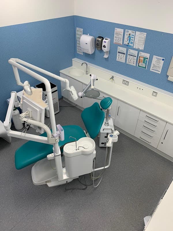 Dental chair with teal upholstery, overhead light, and dental instruments in a clean, modern clinic setting.