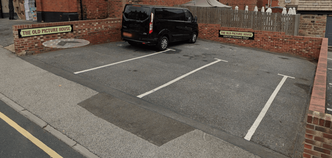 Black van parked in a car park with brick walls, signs for "The Old Picture House," and empty parking spaces.