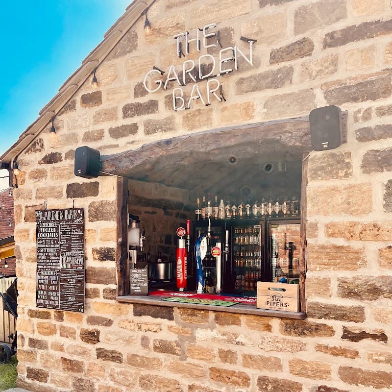 Rustic stone exterior of The Wentworth Arms with a garden bar and a menu board featuring drinks and cocktails.