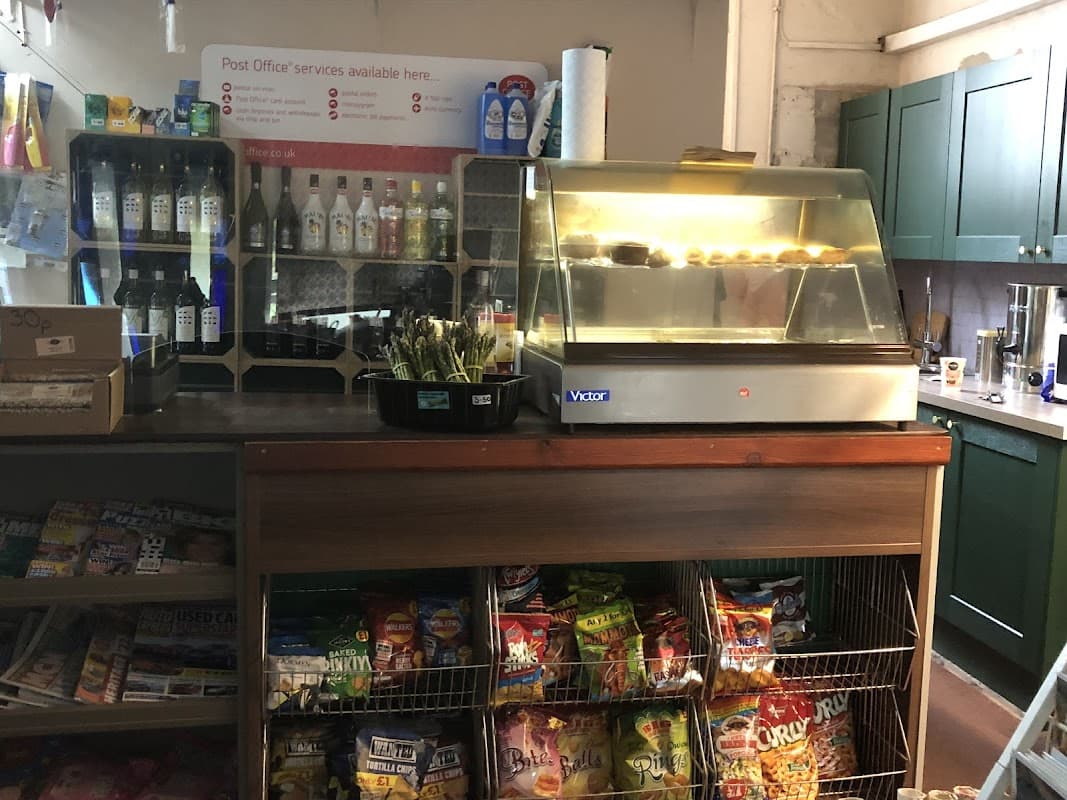 Counter with a glass display case, snacks, drinks, and a variety of magazines in a cozy post office setting.