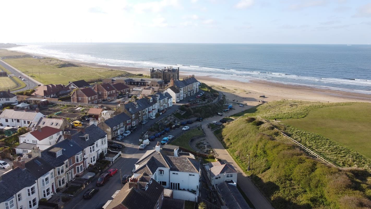 Coastal view of Marske Valley Gardens, featuring sandy beach, houses, and distant wind turbines on the horizon.