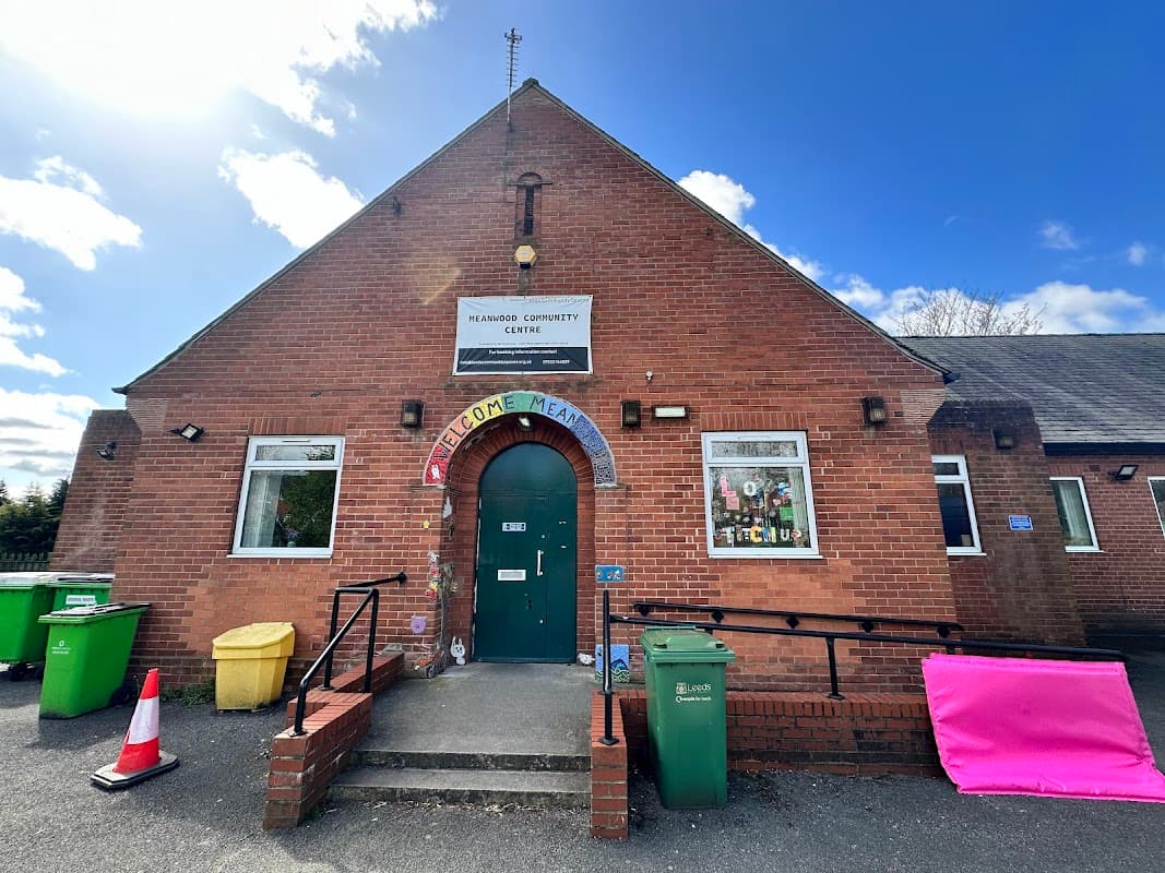 Brick building with a green door, welcoming sign, and colorful bins outside under a blue sky with clouds.
