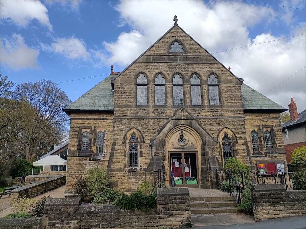 Historic stone church with a pointed arch entrance, surrounded by greenery and a community cafe to the side.