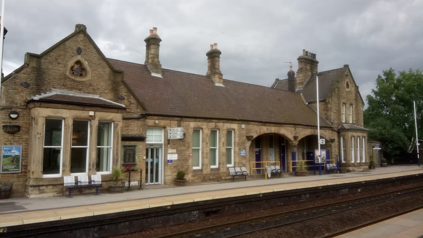 Historic stone building with a tiled roof, benches, and signage, set against a cloudy sky at a bus stop in Mexborough.