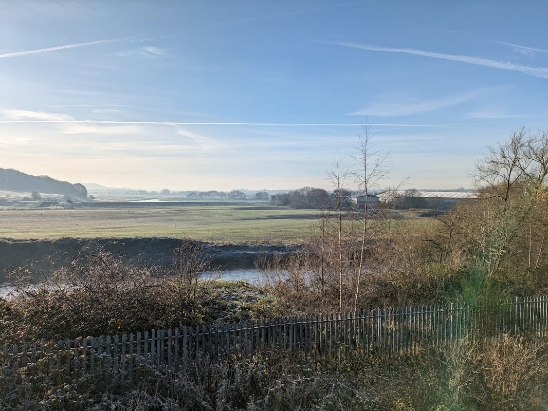 View of a serene landscape with fields and trees, under a clear blue sky near Mexborough Railway Station Car Park.