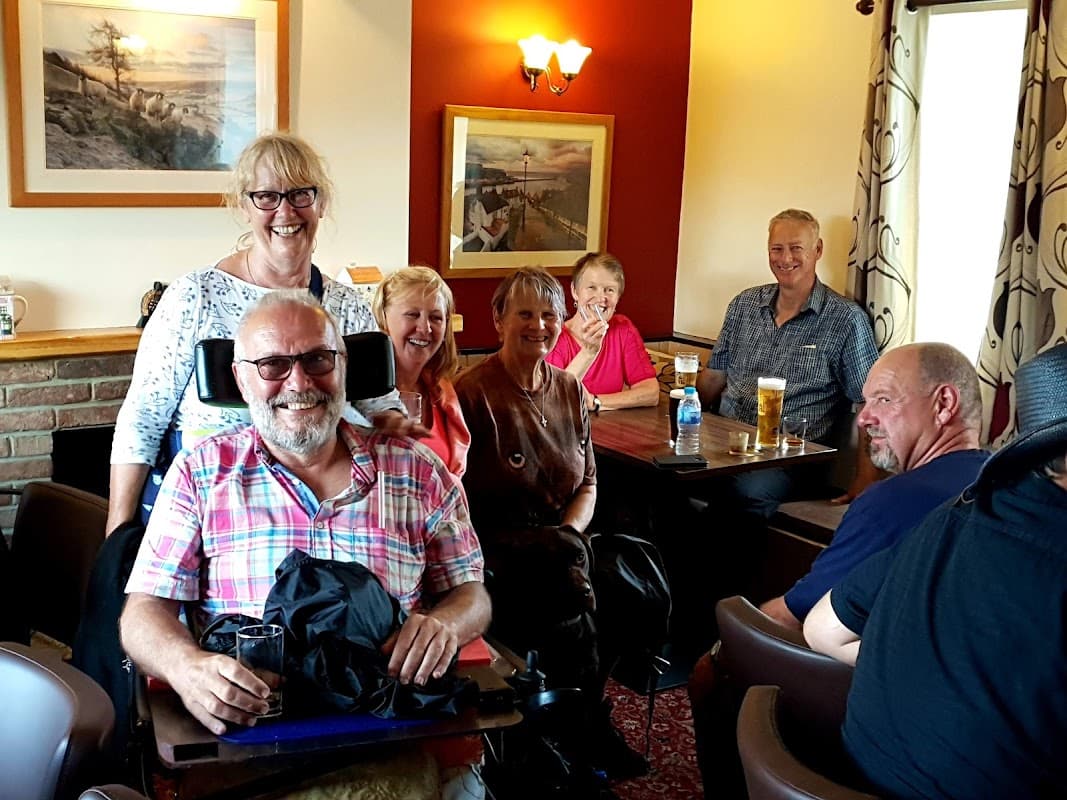 A group of six people smiling inside the White Hart Inn, with drinks on tables and warm lighting.