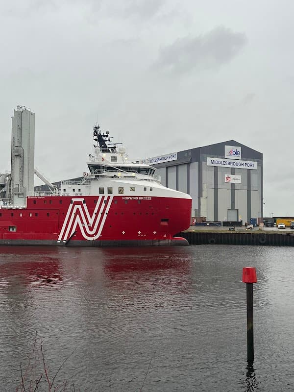 Red and white ship named "NORTHING BREEZE" docked near a large warehouse at Middlesbrough Port under a cloudy sky.