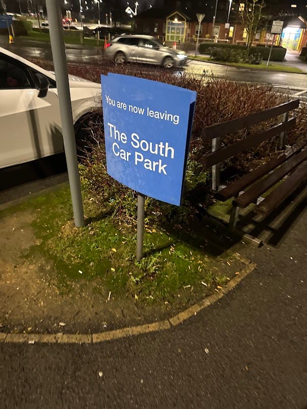 Sign indicating "You are now leaving The South Car Park," surrounded by greenery and parked cars.