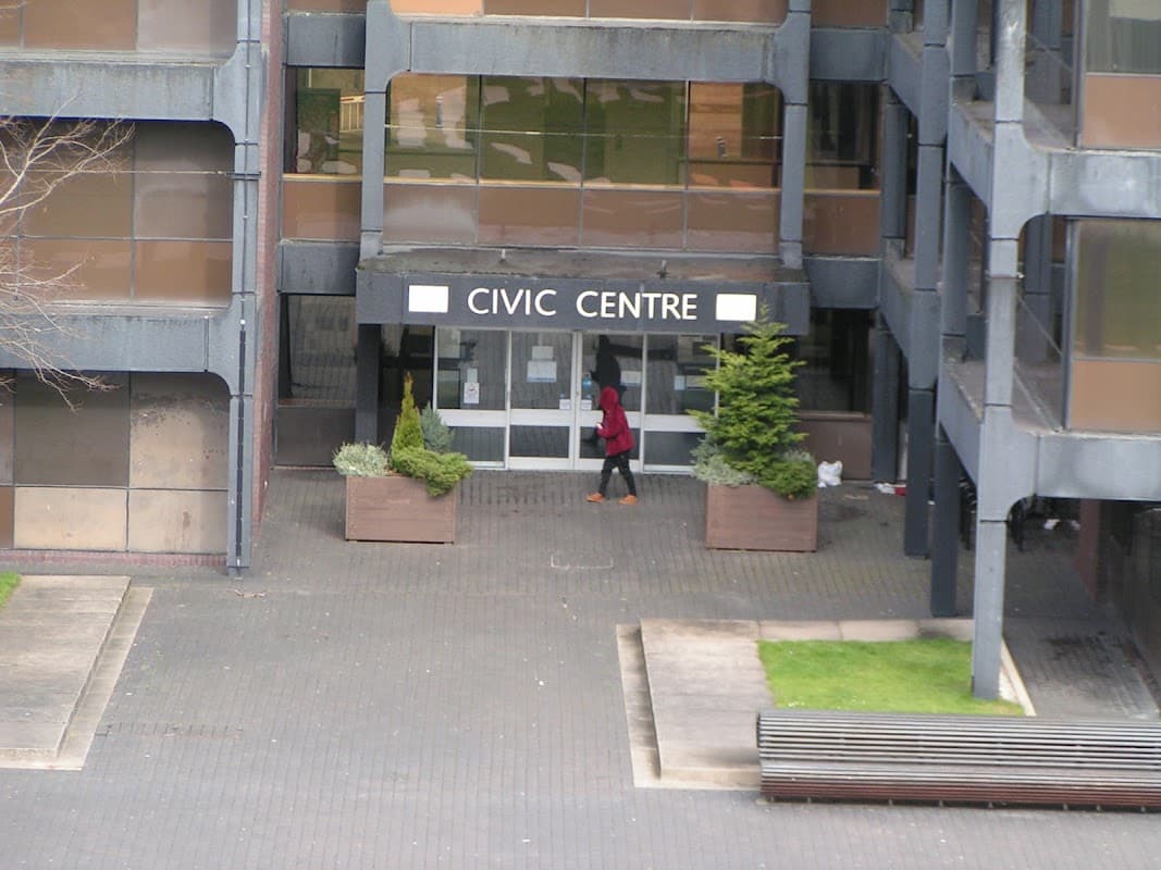 Civic Centre entrance with glass doors, planters, and a person walking by on a paved pathway.