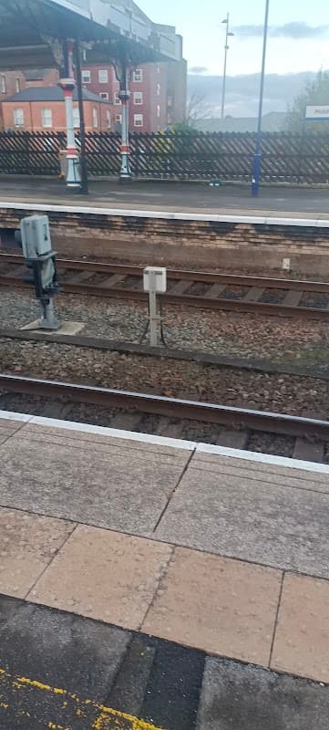 College Reserved Visitors' Car Park sign near train tracks, with a platform and buildings in the background.