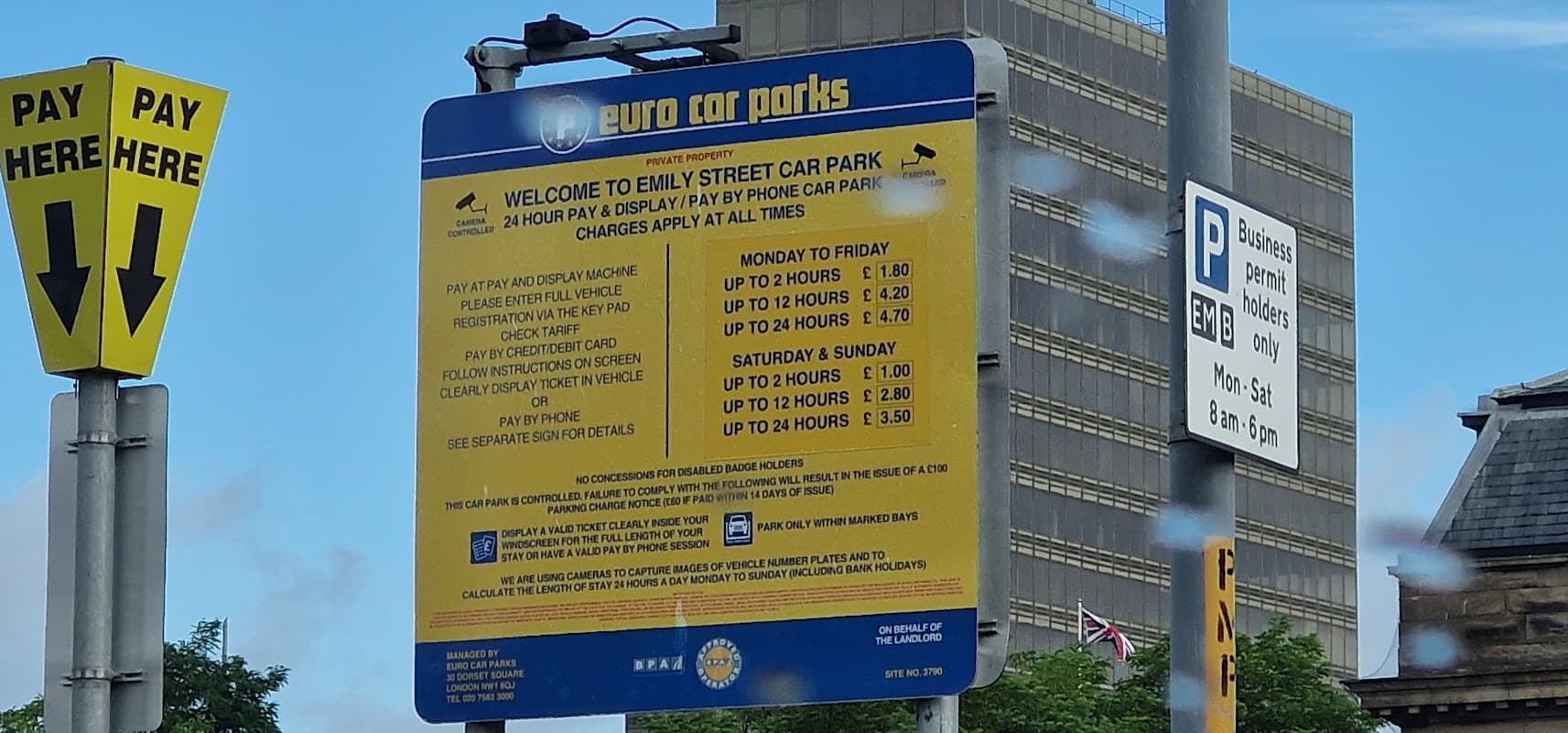 Sign for Emily Street Car Park with parking fees and hours, surrounded by buildings and a clear blue sky.