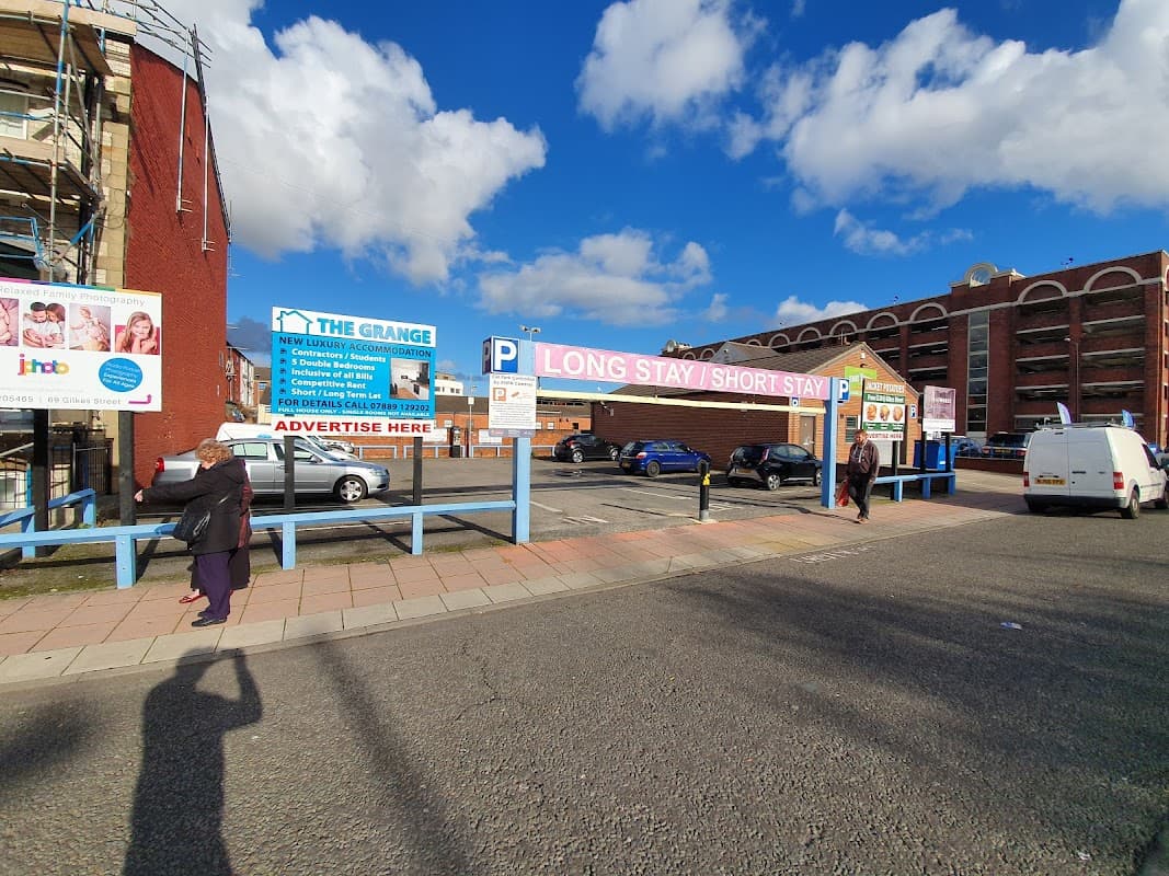 Grange Road Car Park with signage for long and short stays, vehicles parked, and pedestrians walking. Blue sky above.