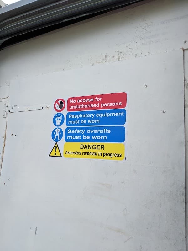 Signage indicating safety precautions for asbestos removal, including warnings and required protective gear.