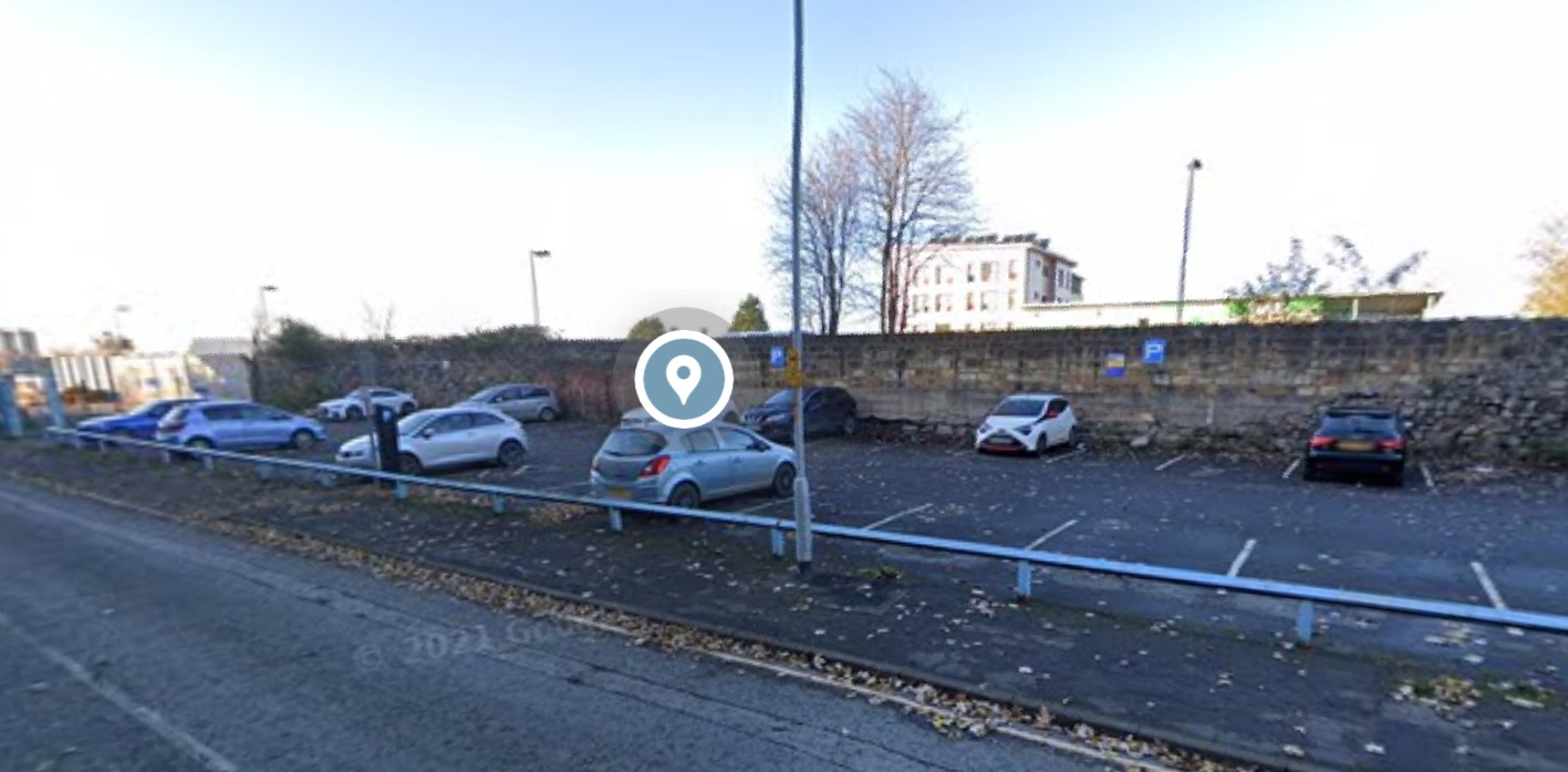 Car park with several parked cars, surrounded by a stone wall and trees, near Middlesbrough Station.