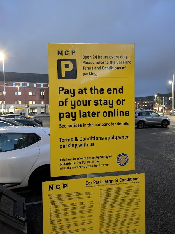 Bright yellow sign detailing parking payment options at NCP Middlesbrough Fry Street, with cars parked nearby.