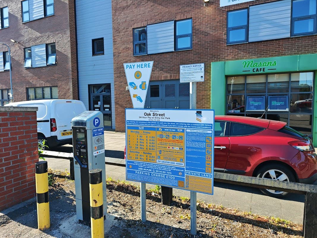 Signage for Oak Street Car Park with parking rates, payment machine, and nearby buildings including Masons Café.