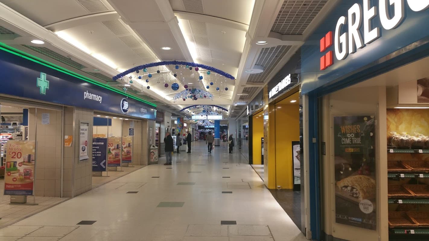 A bustling indoor shopping area with shops, festive decorations, and shoppers walking through the corridor.