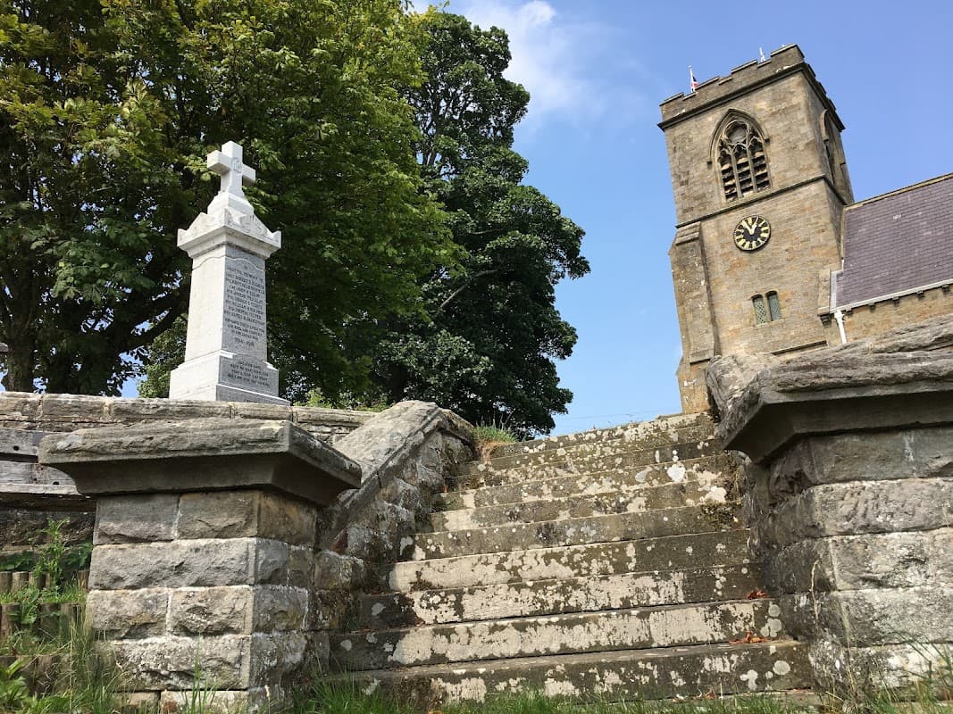 Stone steps lead to a church tower with a clock, surrounded by trees under a clear blue sky.