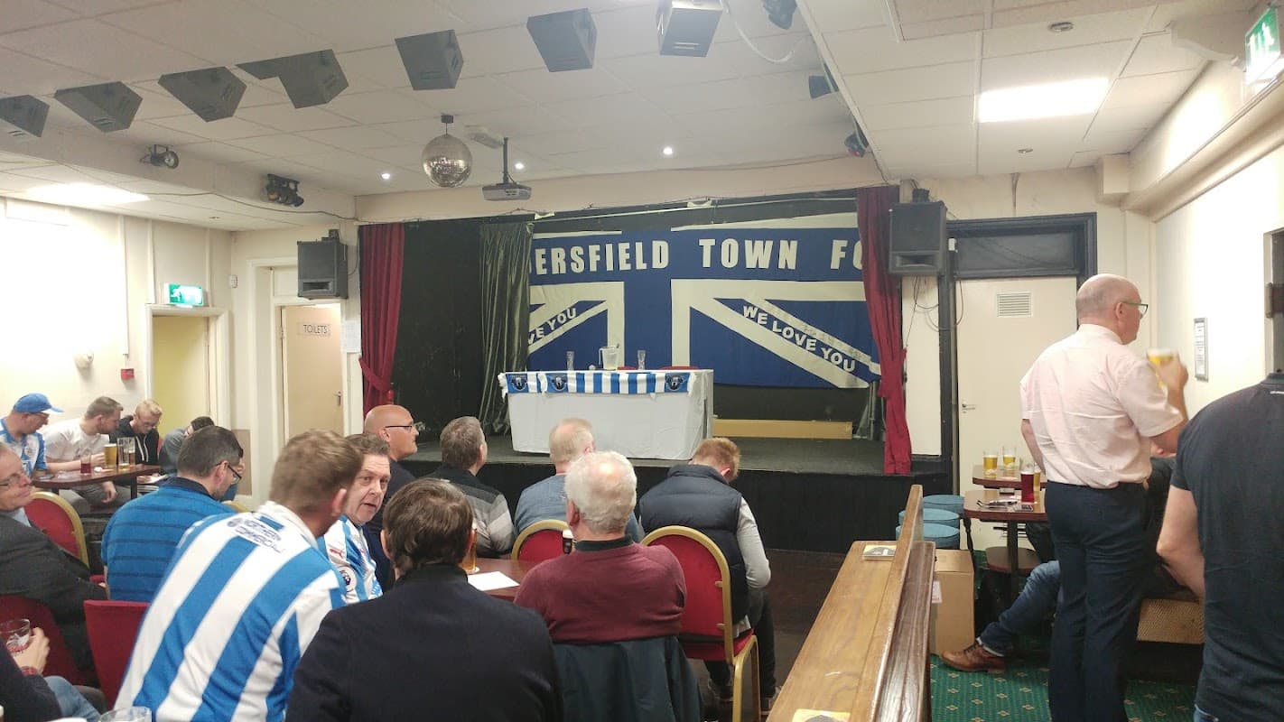 Interior of Middlestown Working Men's Club with a stage, seating, and a banner supporting Huddersfield Town FC.