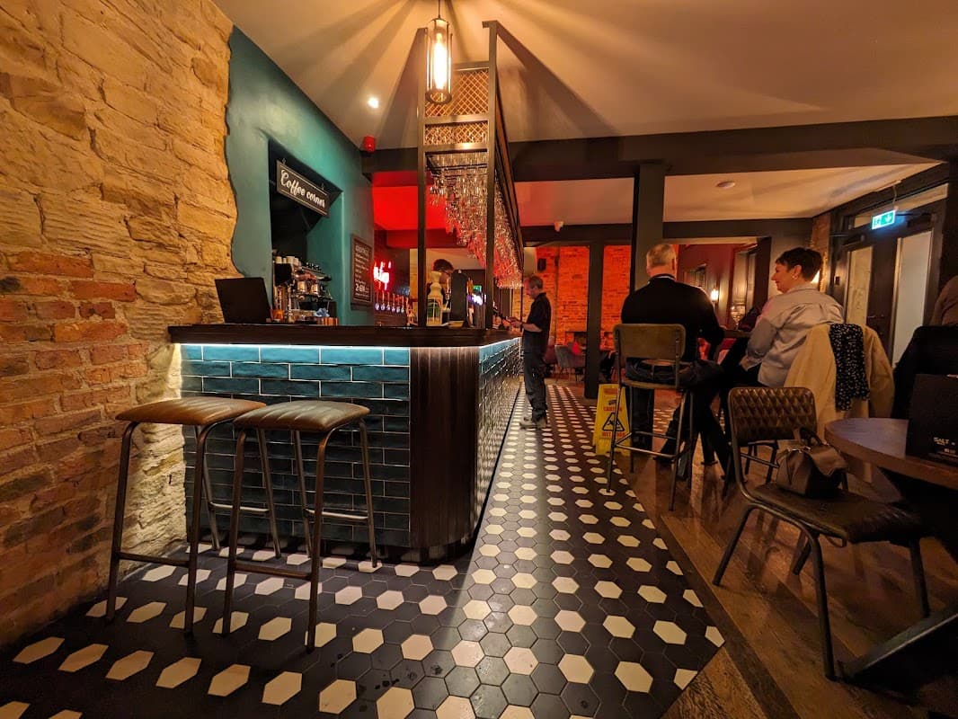 Stylish bar interior with a blue-tiled counter, wooden stools, and patrons enjoying drinks in a cozy atmosphere.