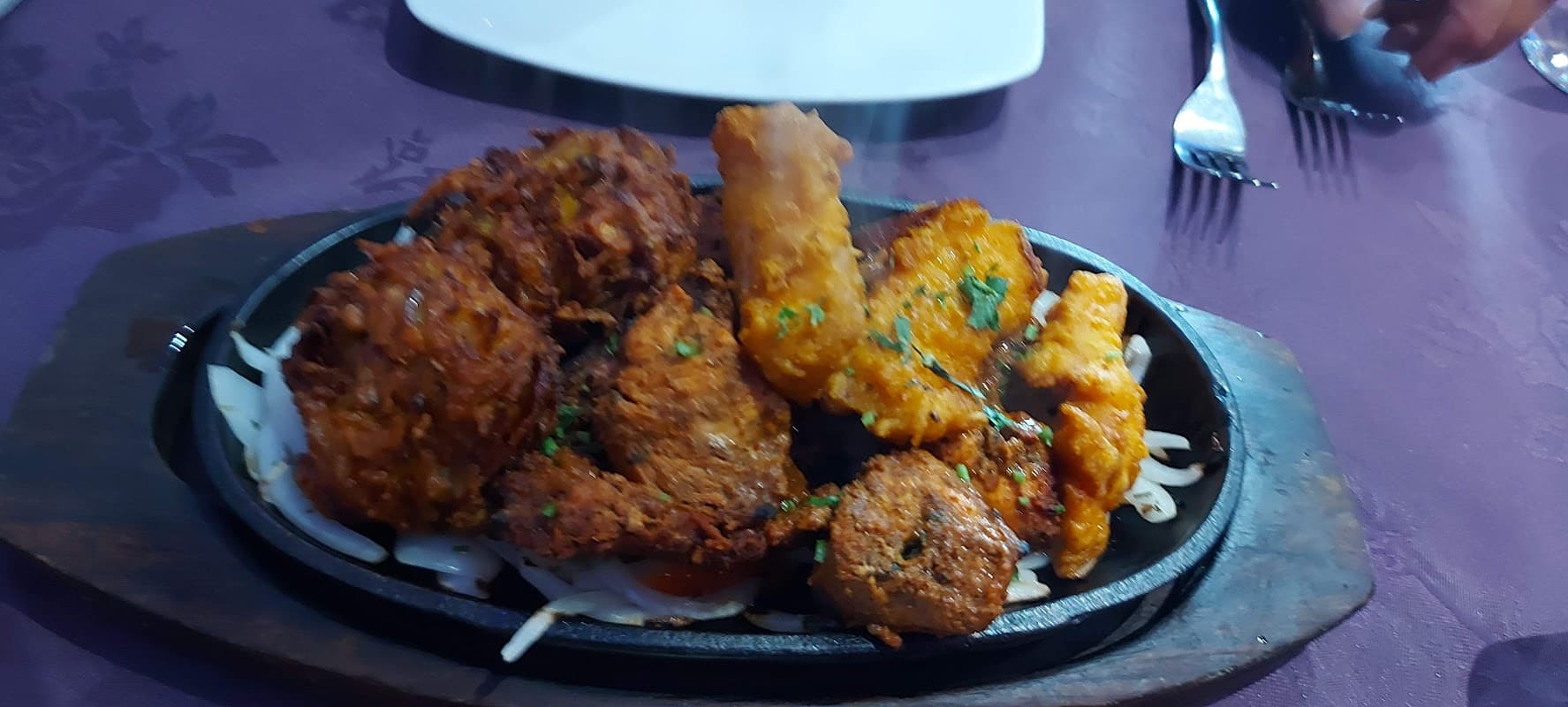Sizzling platter of assorted fried appetizers, garnished with herbs, on a wooden serving board.