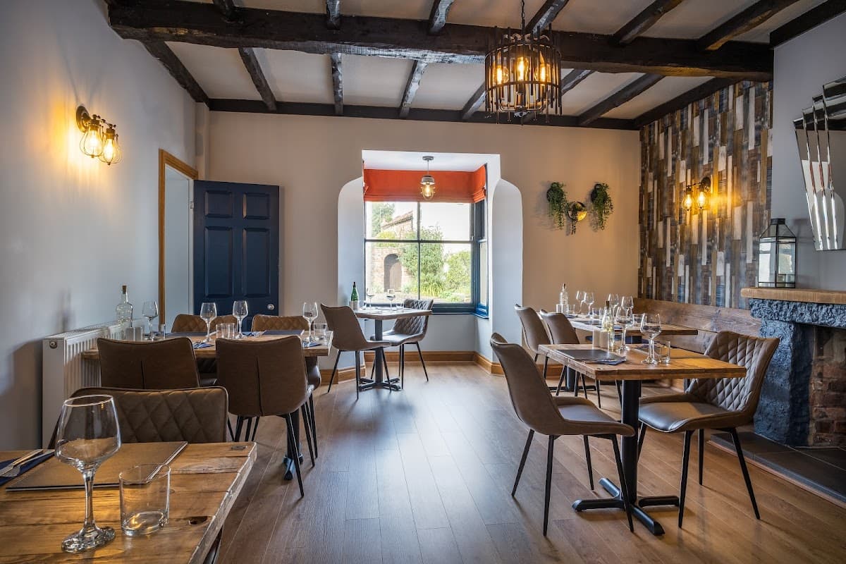 Cozy bar interior with wooden beams, tables set for dining, and a large window overlooking greenery.