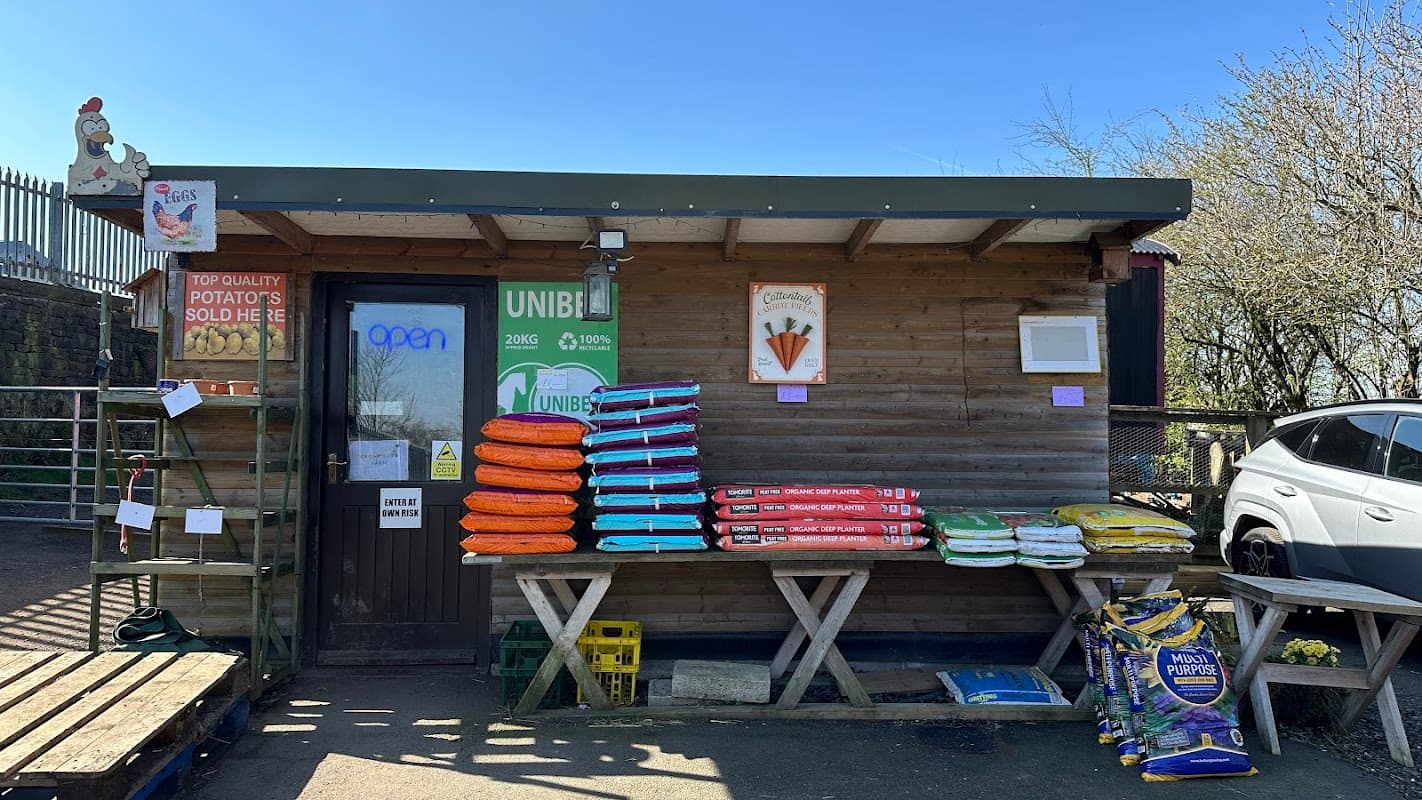 Rustic farm shop with colorful bags of feed, a sign reading "open," and a sunny blue sky in Millhouse Green.