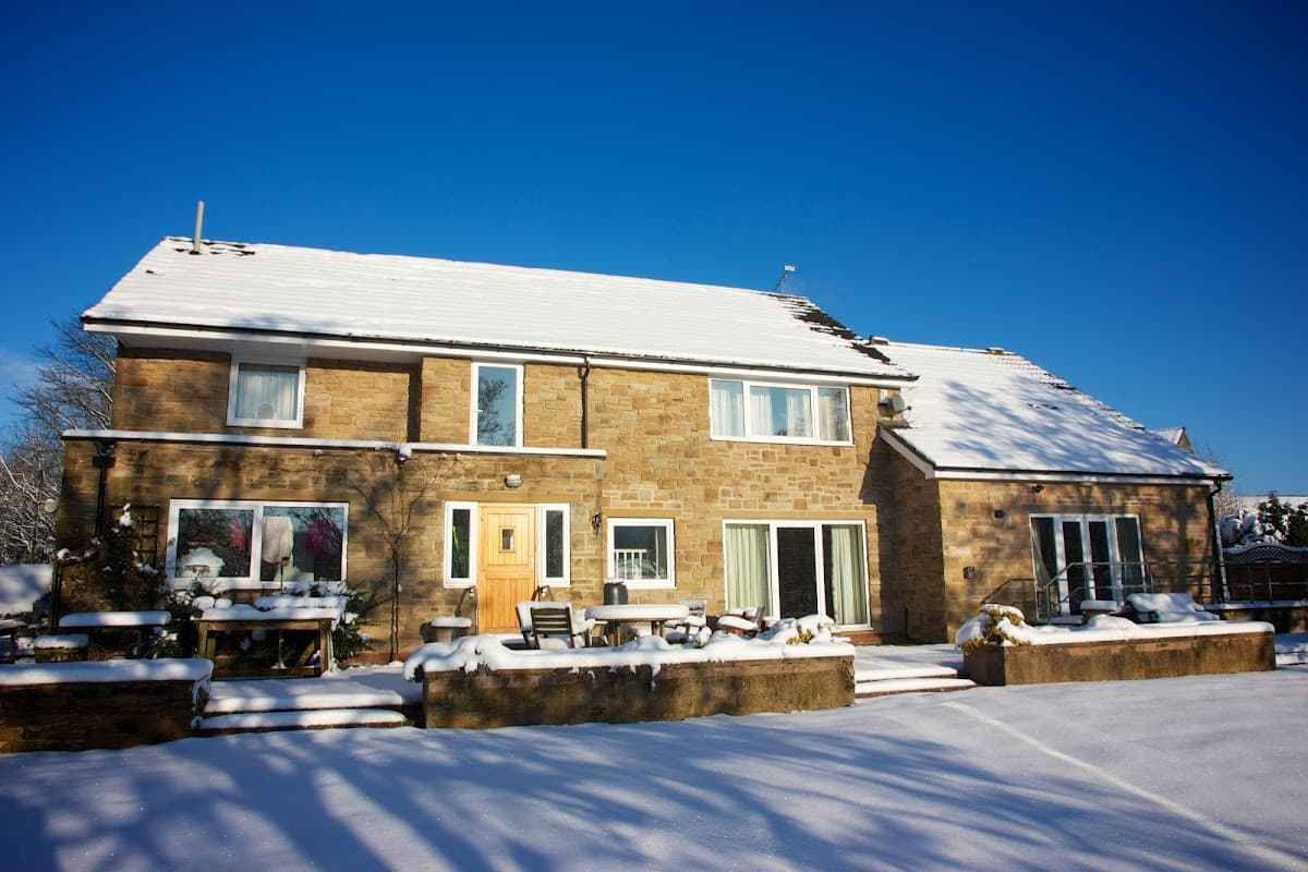 Stone building covered in snow, with a clear blue sky, surrounded by a snowy landscape and outdoor seating.