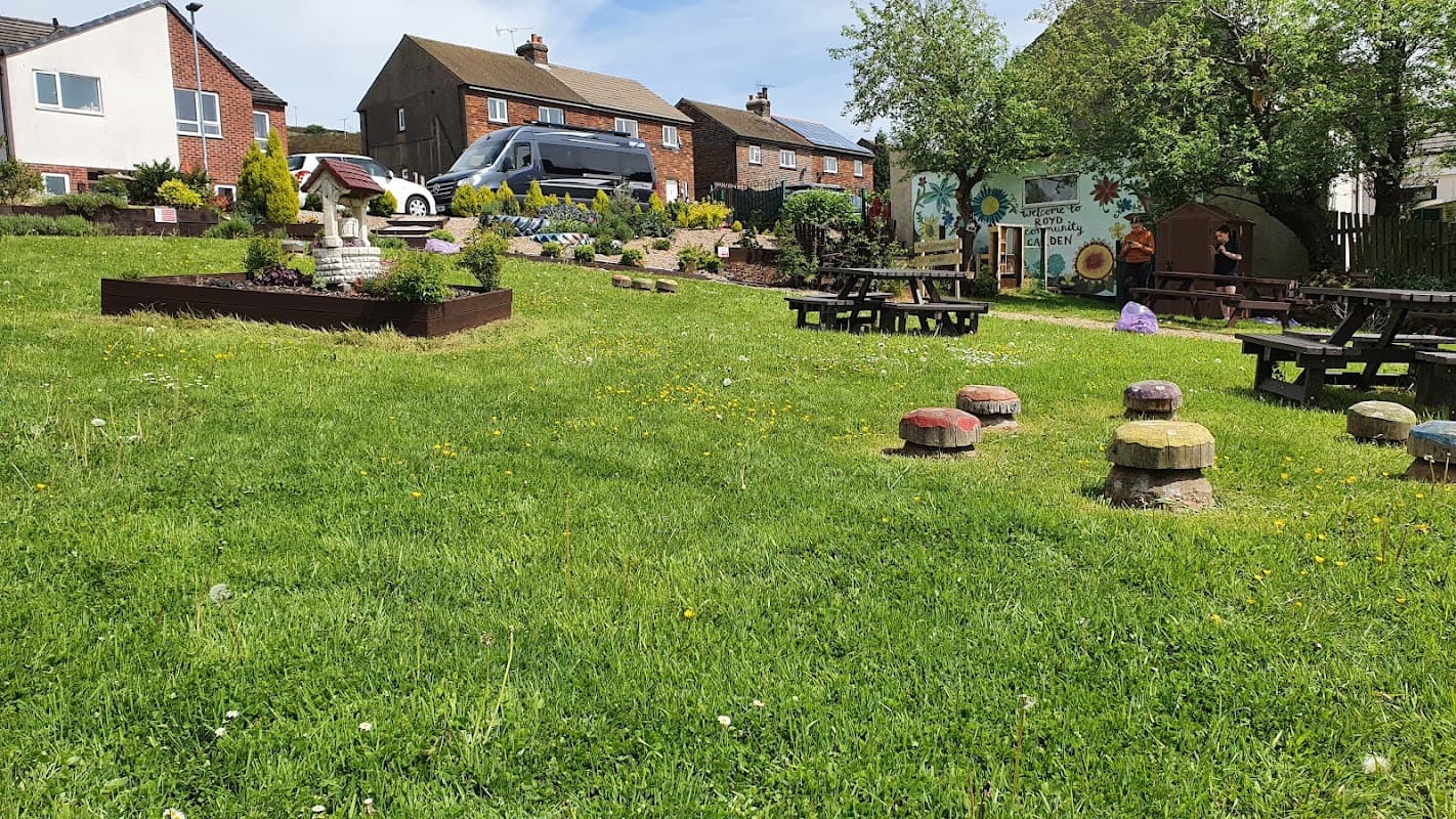 Community garden with colorful seating, green grass, flower beds, and a mural in a residential area.