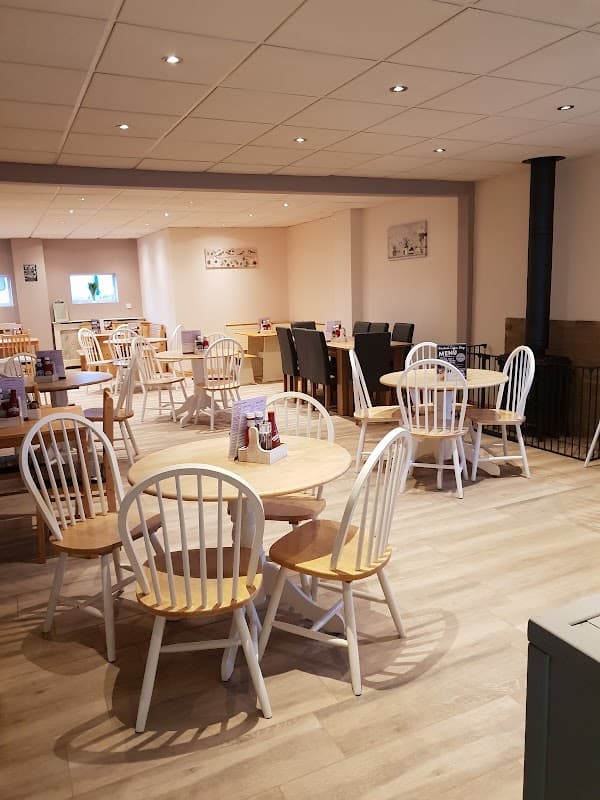 Cozy coffee shop interior with wooden tables, white chairs, and a warm atmosphere, featuring a stove and soft lighting.