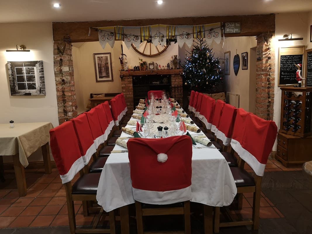 Long dining table set for a festive meal, with Santa hat chair covers and a decorated Christmas tree in the background.
