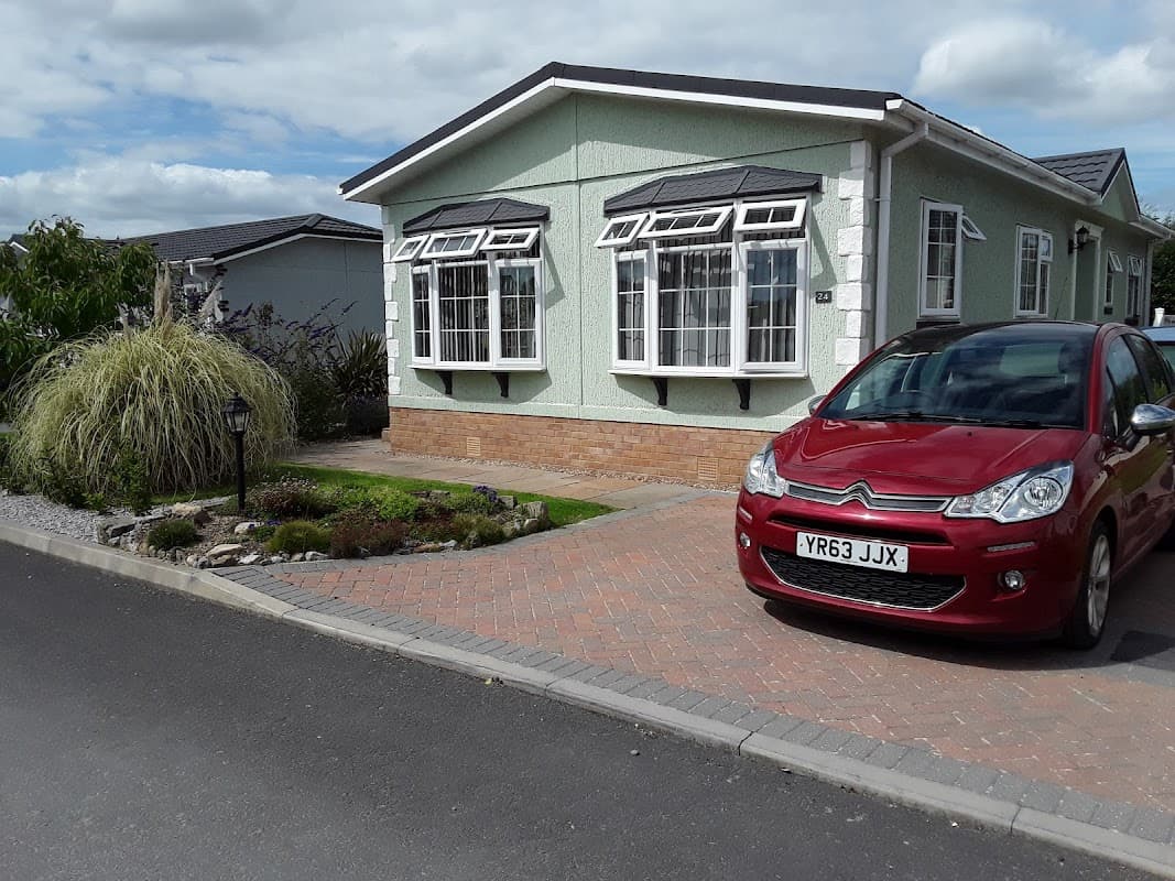 Green hotel building with large windows, landscaped garden, and a red car parked on a brick driveway.