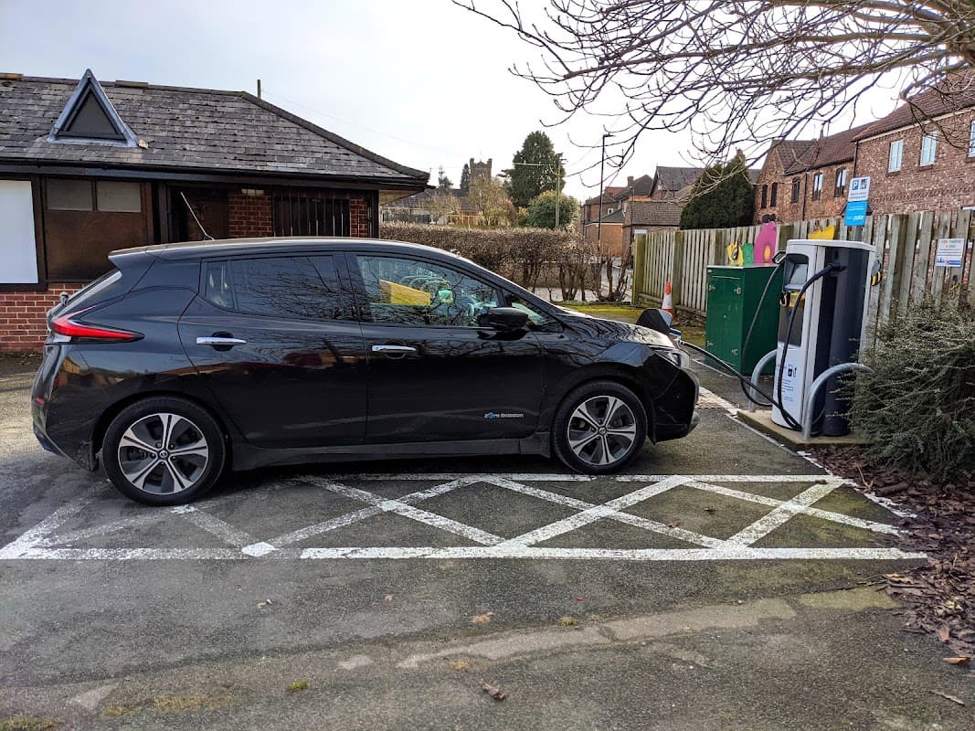 Black electric car parked at a bp pulse charging station in Minskip, Yorkshire, with buildings and trees in the background.