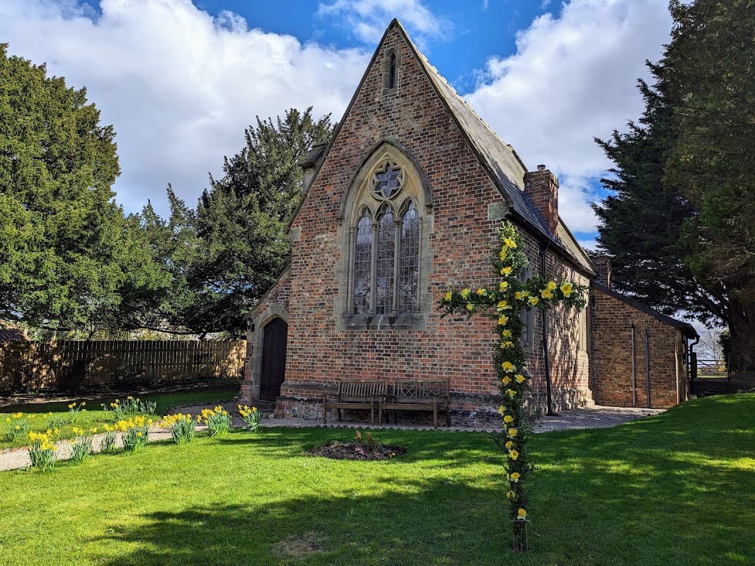 Minskip Village Hall features a brick building with stained glass windows, surrounded by trees and blooming daffodils.