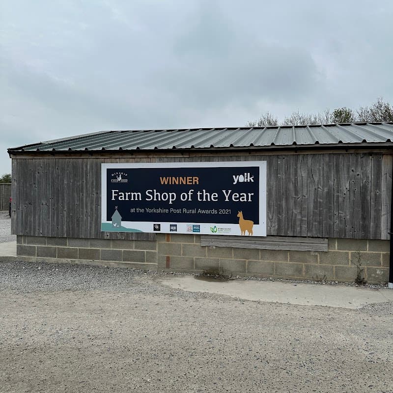 Wooden building with a metal roof, featuring a large sign announcing "Winner Farm Shop of the Year" in Minskip.