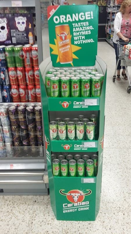Display stand for Caraboo energy drinks, featuring vibrant green cans and a sign promoting the orange flavor.