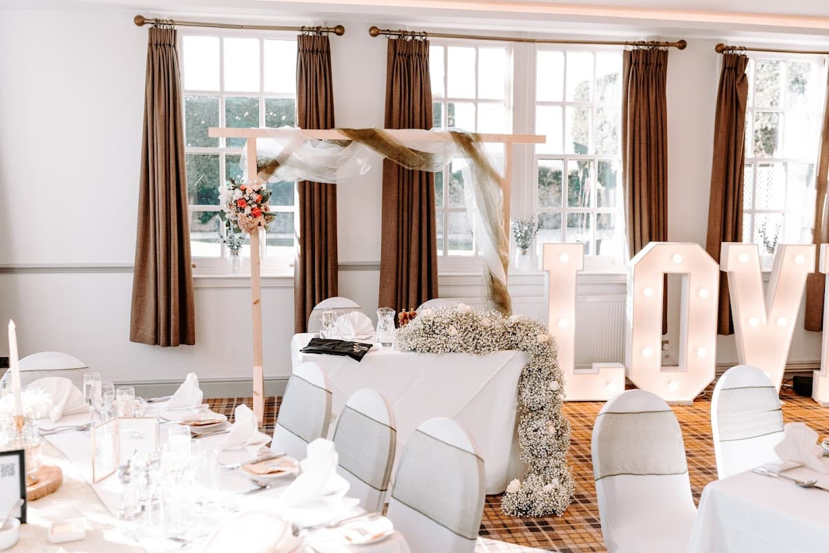 Elegant floral arrangements with a decorative arch and illuminated "LOVE" sign in a bright, stylish venue.