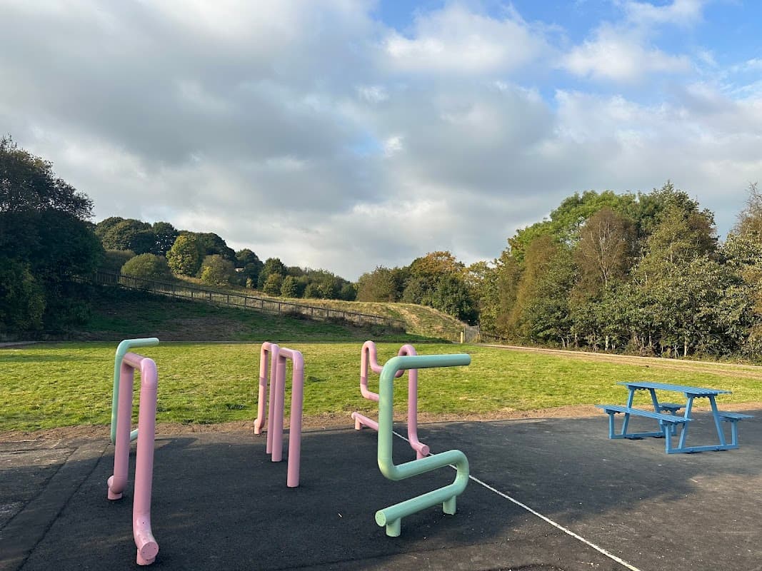 Colorful playground structures and a picnic table set against a grassy area and trees under a cloudy sky.