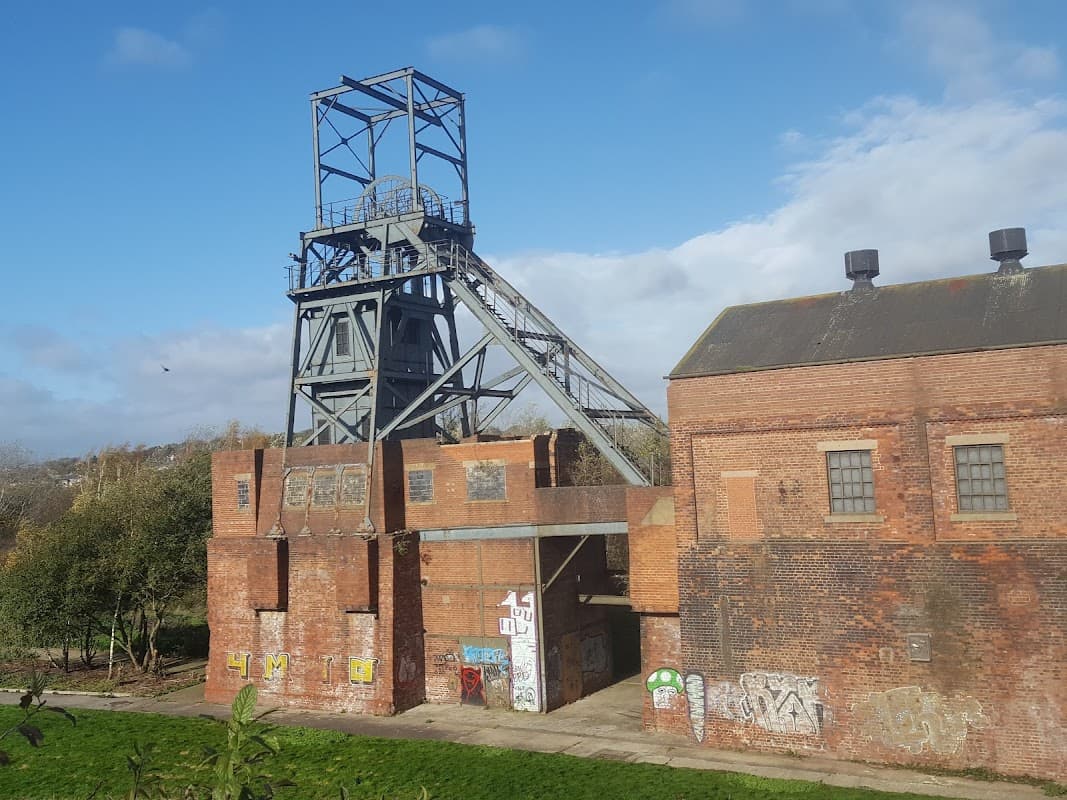 Old brick industrial building with a tall coal mine tower, surrounded by greenery under a blue sky.