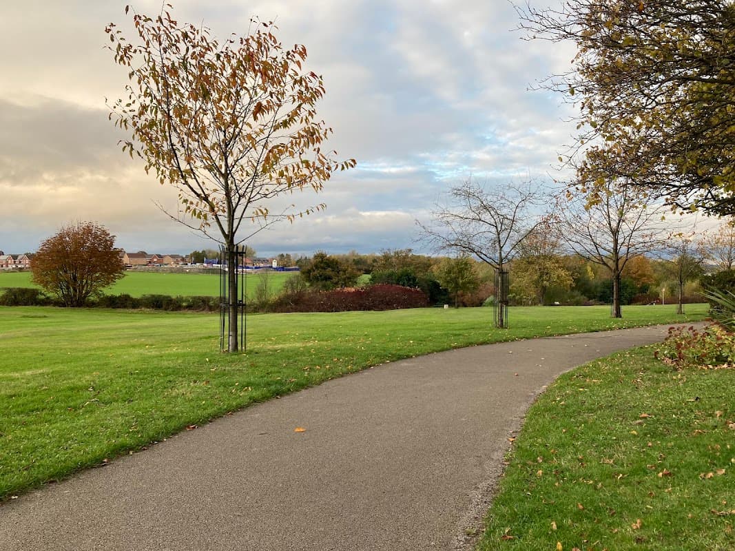 Pathway winding through green grass with young trees, under a cloudy sky in Monk Bretton Park, Yorkshire.