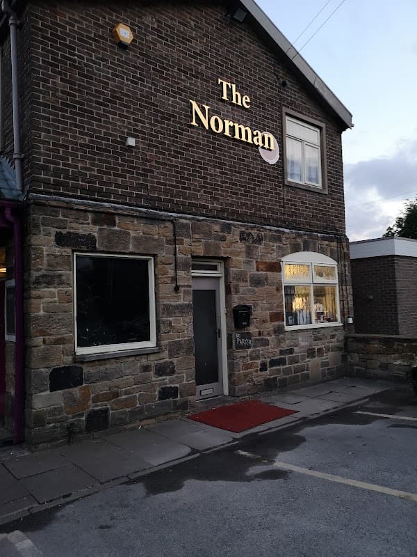 Brick building with "The Norman" sign, large window, and a red doormat at the entrance.