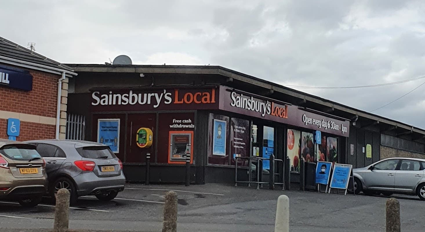 Sainsbury's Local storefront in Monk Bretton, Yorkshire, featuring large signage and a cash withdrawal machine.