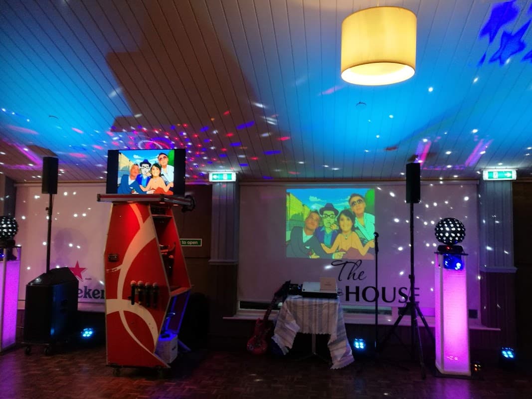 A vibrant bar interior with colorful lights, a karaoke machine, and screens displaying animated characters.