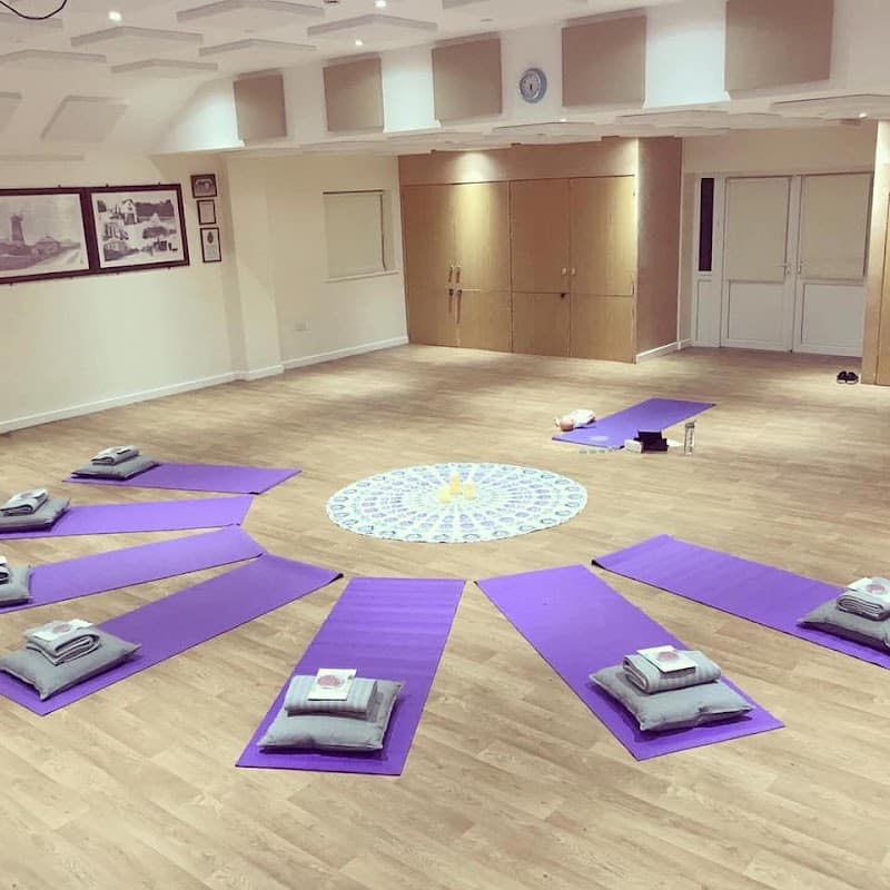 Yoga mats arranged in a circular pattern around a central mandala on a wooden floor in a spacious room.