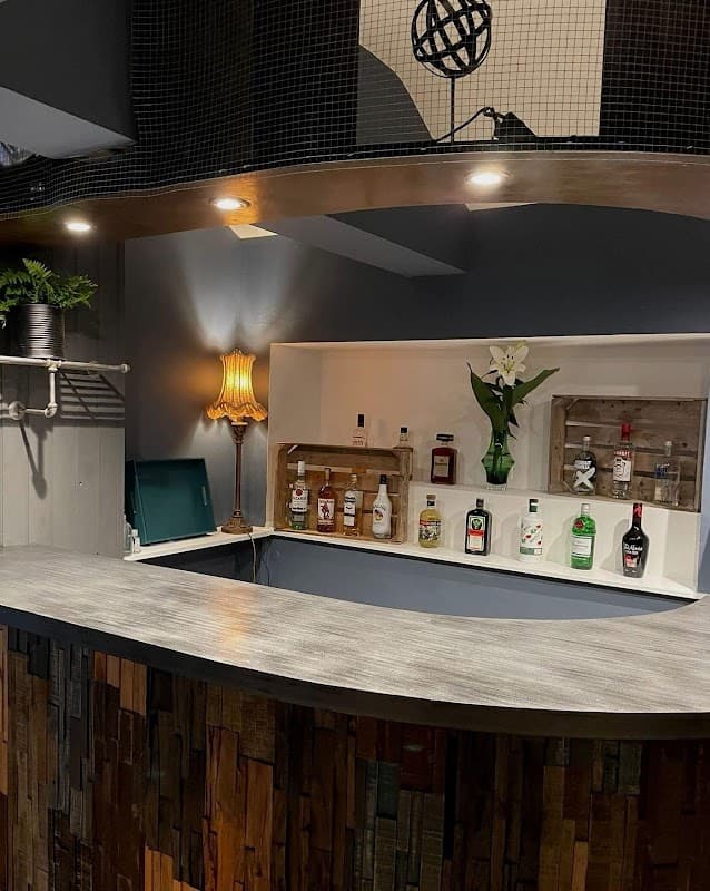 Modern bar area featuring a curved counter, various bottles, a lamp, and decorative plants.