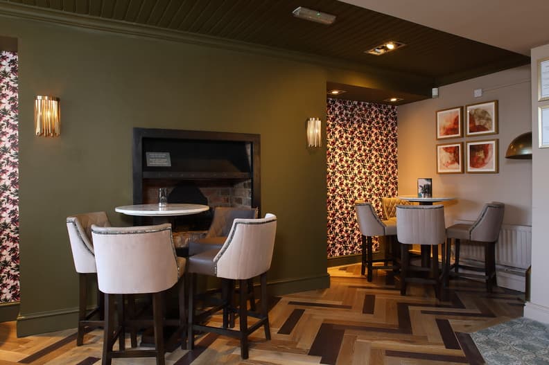 Cozy pub interior featuring a brick fireplace, floral wallpaper, and stylish seating arrangements.