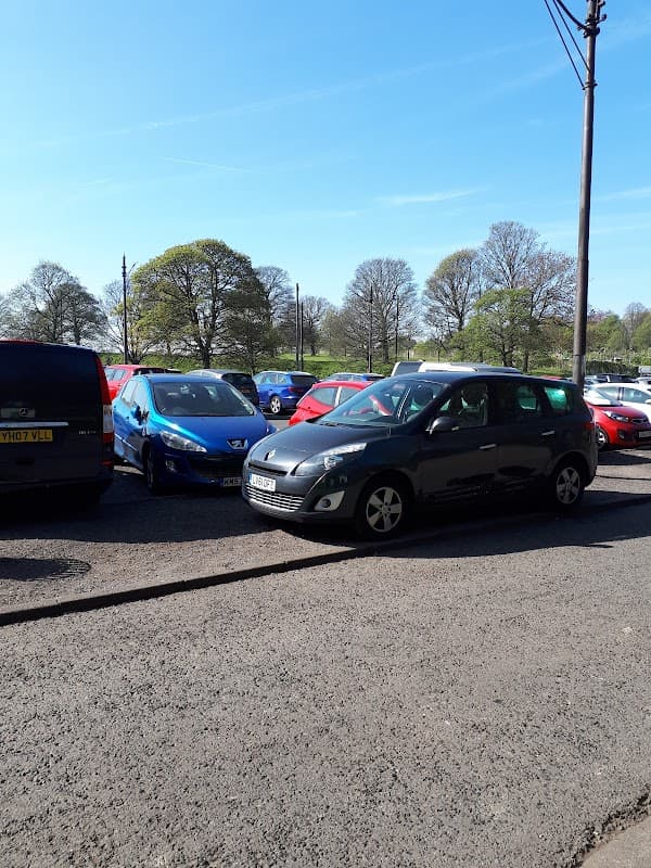Main car park at Roundhay Park, featuring several parked cars and trees in the background under a clear blue sky.