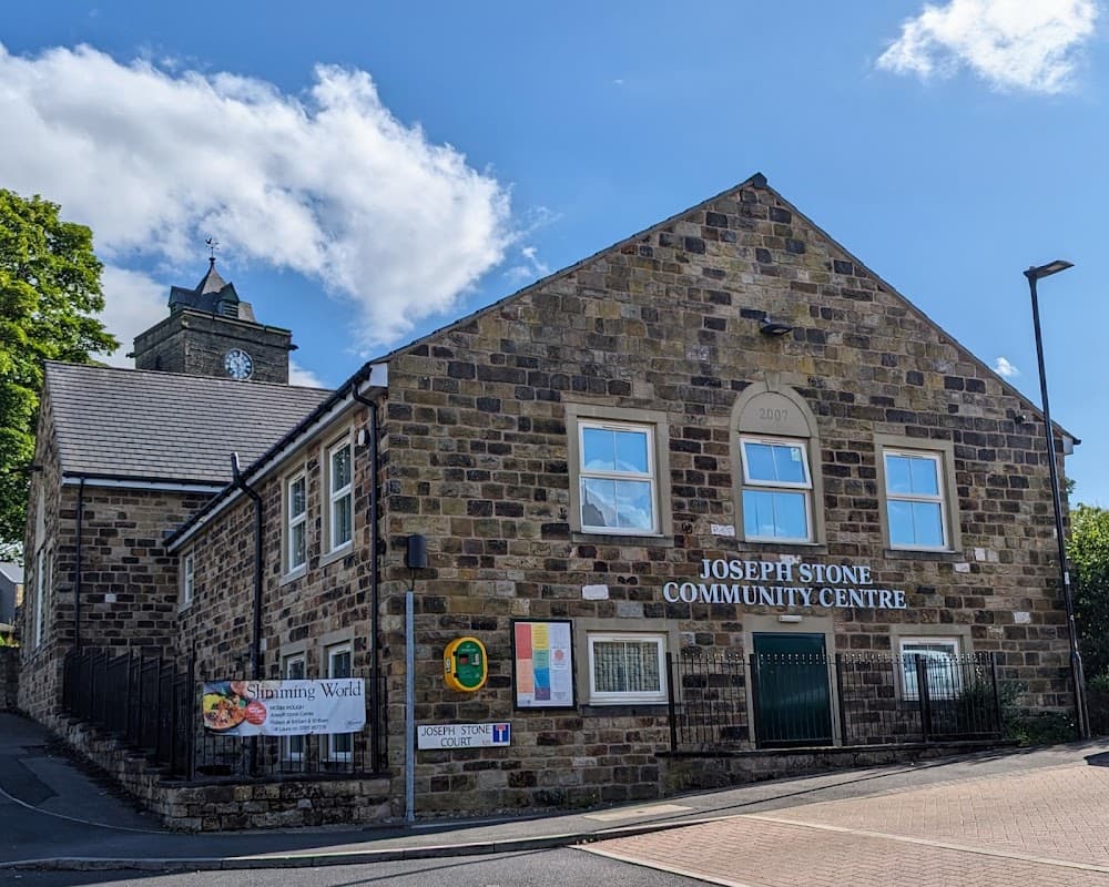Joseph Stone Community Centre, a stone building with a clock tower, signage, and surrounding greenery in Mosborough.