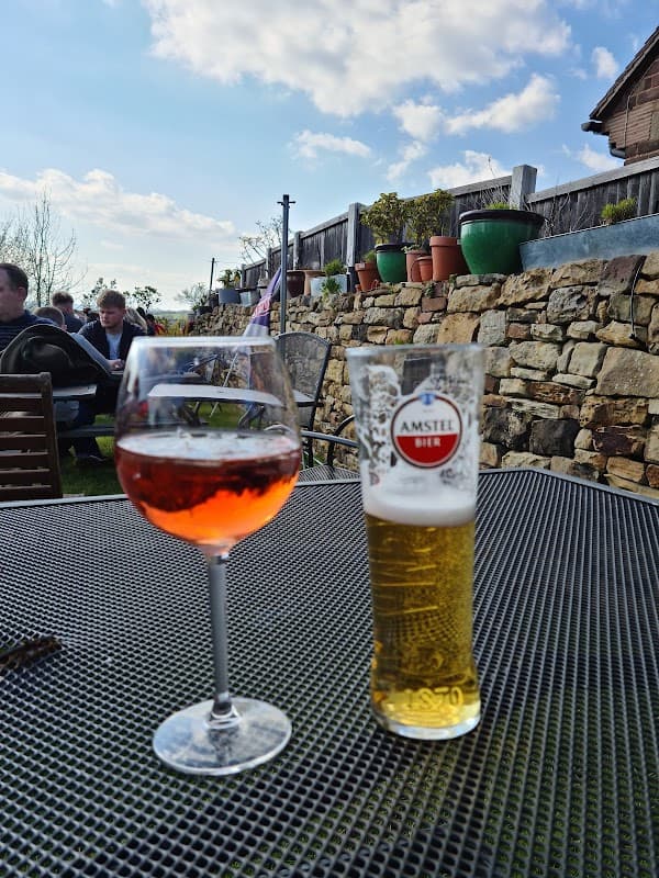 A glass of rosΓ© wine and a pint of Amstel beer on a patio table, with a stone wall and potted plants in the background.
