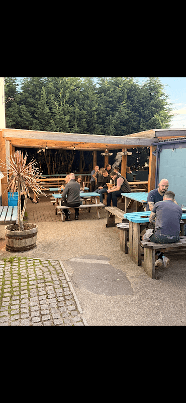 Outdoor seating area at The Queen Hotel, featuring wooden tables, patrons socializing, and greenery in Mosborough, Yorkshire.